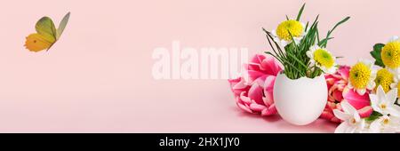 Easter creative composition. Spring flowers, Easter egg and butterflies on pink banner. Easter card. Stock Photo