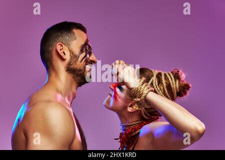 Beautiful young acrobats or gymnasts with colorful face painting on pink blue gradient background. Professional ballet couple dancing, Emotional duet Stock Photo