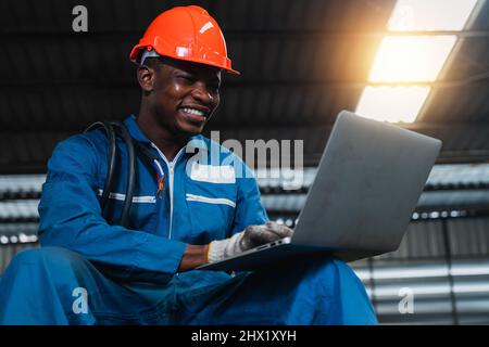 Happy African electrical engineer man working on laptop by checking and electrical  yearly inspection and maintenance  in factory Stock Photo