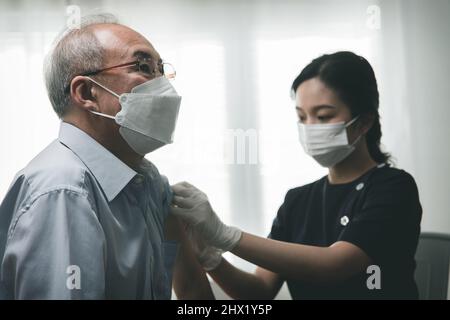 old Asian man vaccinate with doctor woman, giving shot to senior patient, Covid-19 vaccine injection concept Stock Photo