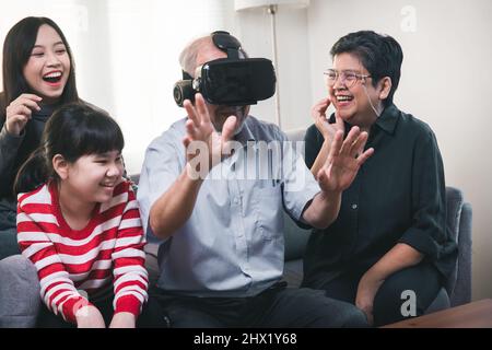 old Asian man or grandfather wearing VR glasses and big family have fun with him Stock Photo