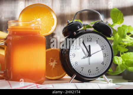 The alarm clock indicates 12.00. and Fresh vegetable juice in a glass. A glass of delicious freshly squeezed fruit juice. Background with copy space Stock Photo