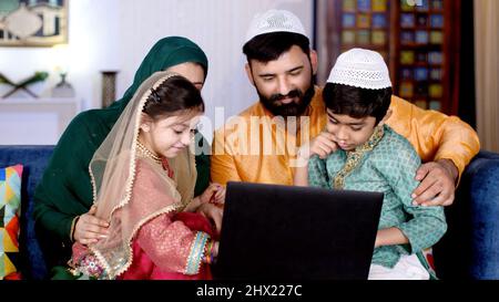 Nuclear Muslim family in India, Cute siblings in an ethnic dress. A cheerful Muslim family using a laptop together - modern technology, an electronic Stock Photo