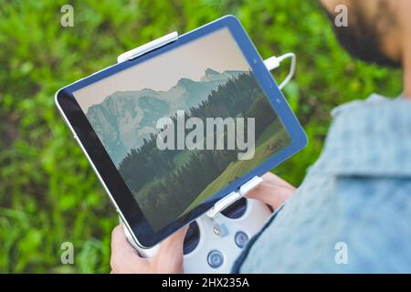 Young man flying drone on amazing mountain landscape. Man operating a drone with remote control taking aerial photos and videos. Stock Photo