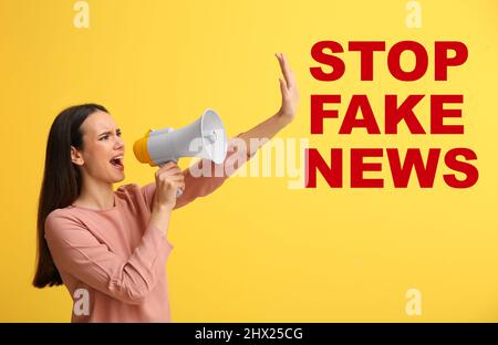 Screaming young woman with megaphone and text STOP FAKE NEWS on yellow background Stock Photo
