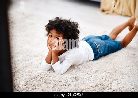 This movie is getting more interesting by the minute. Cropped shot of an adorable little boy lying down on a carpet and watching tv at home. Stock Photo