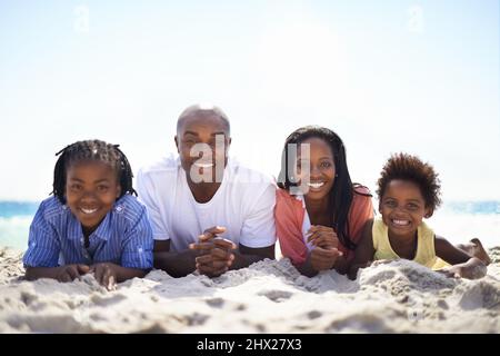 All lined up for summer fun. An african-american family lying in a line on the beach. Stock Photo