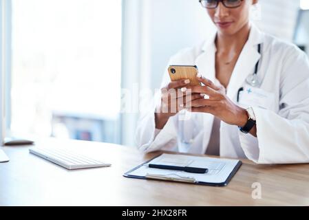 Smart apps for a smart doctor. Shot of a young doctor using a smartphone in her consulting room. Stock Photo