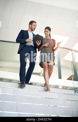 Walk with me. Full length shot of two colleagues walking down the stairs in their office. Stock Photo
