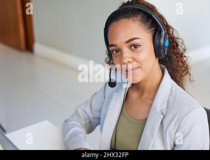 A wider shot of a young woman with a headset in the office slightly smiling Stock Photo
