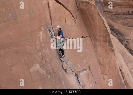 A female lead climber sets up a rope anchor at the top of the Flakes of Wrath, Wall Street near Moab, Utah. Stock Photo