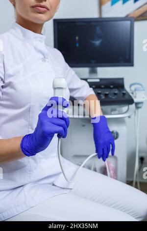 A young woman is an intern doctor, she is in a white suit and medical gloves holding an ultrasound probe on her hands. ultrasound diagnostics. selecti Stock Photo