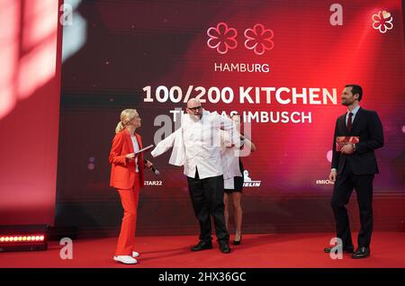 09 March 2022, Hamburg: Michelin-starred chef Thomas Imbusch (M) of Hamburg's '100/200 Kitchen' restaurant receives the coveted jacket for a two-star chef during the 2022 Michelin star awards ceremony for German restaurants at the Chamber of Commerce. According to the director of the 'Guide Michelin', the restaurant at the Elbbrücken had intensively used the Corona period to significantly improve the culinary offer. It was therefore awarded two stars. Although the Corona pandemic has caused problems for many restaurateurs, the forced breaks have spurred the country's top chefs on to top perfor Stock Photo