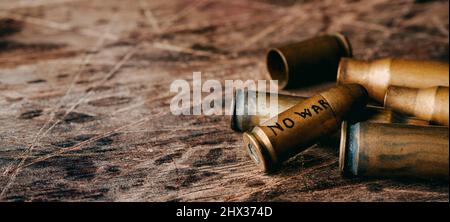 the text no war written in a bullet on a pile of bullet shells on a rustic surface, in a panoramic format to use as web banner or header Stock Photo