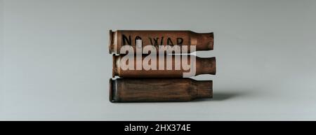 the text no war written in a used bullet shell on top of a pile of bullet shells on a gray background, in a panoramic format to use as web banner or h Stock Photo