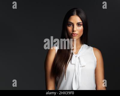 Makeup is art. Beauty is spirit. Portrait of an attractive young woman wearing a white blouse and posing against a dark background in the studio. Stock Photo