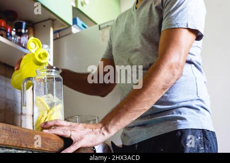 High angle view of unrecognizable brunette man standing by the kitchen counter at home preparing a lemonade. Stock Photo