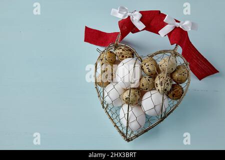 Chicken and quail eggs in a heart shaped woven metal wire box tied Stock Photo