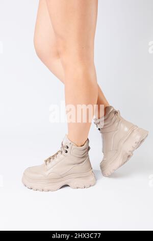 Female legs in beige leather shoes from the new collection on a white background female legs in fashionable shoes made of eco-leather spring 2022. Stock Photo