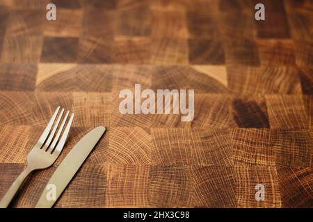 A dining gold fork and knife sitting on top of an empty butcher block counter top in a kitchen Stock Photo