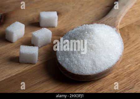 Granulated sugar and sugar cubes in wooden spoon on wooden background Stock Photo
