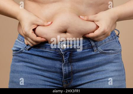 Caucasian fat woman touching overweighted belly with hands wearing blue jeans. Visceral fat. Body positive and accepting yourself. Sudden weight gain Stock Photo