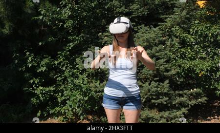 Female in virtual reality glasses controls the device with his hands against the background of green trees Stock Photo