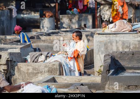 A dhobi wallah (washerman) works gathering up clothes in a typical concrete wash pen, Mahalaxmi Dhobi Ghat, a large open air laundry, Mumbai, India Stock Photo