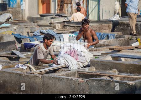 A dhobi wallah (washerman) works washing clothes in a typical concrete wash pen in Mahalaxmi Dhobi Ghat, a large open air laundromat, Mumbai, India Stock Photo