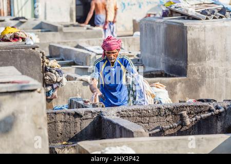 A dhobi wallah (washerman) works washing materials in a typical concrete wash pen in Mahalaxmi Dhobi Ghat, a large open air laundromat, Mumbai, India Stock Photo