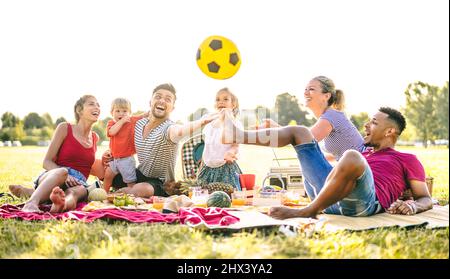 Happy multiracial families having fun with cute kids at pic nic garden party - Multicultural joy and love concept with mixed race people playing toget Stock Photo