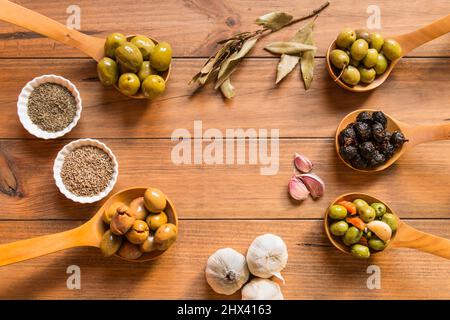 Still life with different varieties of olives, presented in wooden ladles, seasoned with different traditional dressings. Traditional homemade dressin Stock Photo