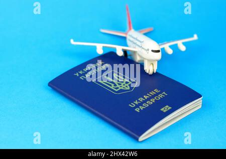 Ukrainian passport and a toy plastic plane on a blue background. Departure of Ukrainians abroad Stock Photo