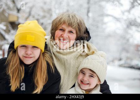 Joyful family grandmother with grandchildren in warm clothes playing outdoors in winter park, enjoying frosty and snowy weather, children actively spe Stock Photo