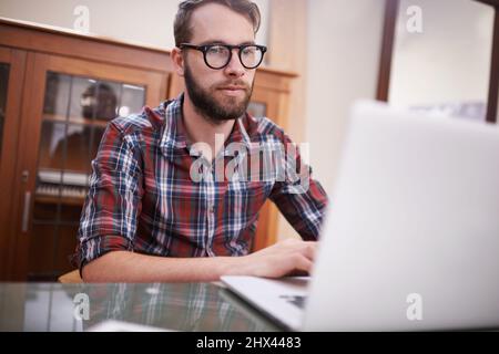 Using all the latest tech. Shot of a handsome young hipster working on a laptop. Stock Photo