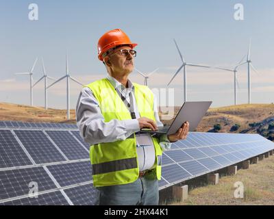 Male engineer working with a laptop computer on a field with solar panels and wind turbines Stock Photo