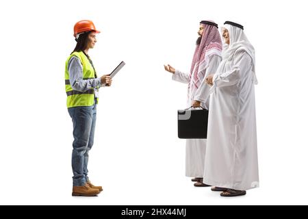 Full length profile shot of arab men talking to a young female engineer with a safety vest and hardhat isolated on blue background Stock Photo