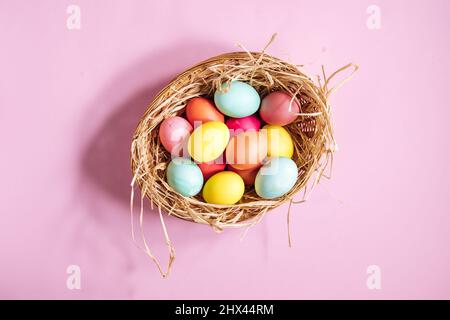 Colorful easter eggs in yellow basket with straw on pink background. Top view of Happy Easter postcard concept Stock Photo