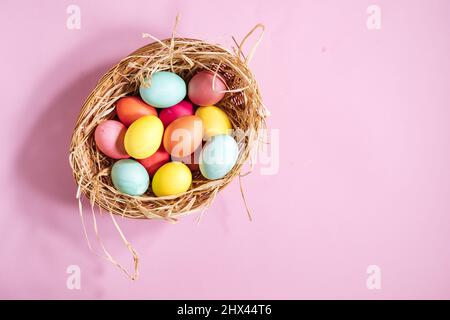 Colorful easter eggs in yellow basket with straw on pink background. Top view of Happy Easter postcard concept Stock Photo