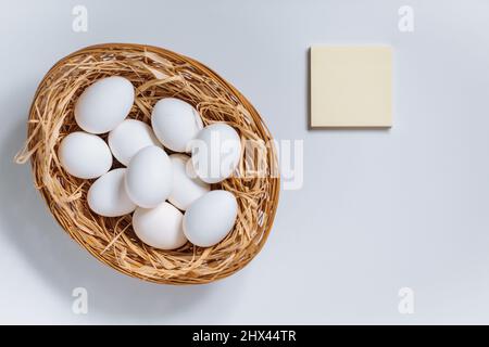 White easter eggs in yellow basket with straw on white background. Top view of Happy Easter postcard concept Stock Photo
