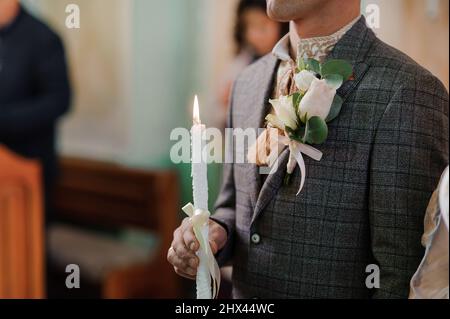 The bride and groom hold shining candles during the ceremony in the church. Hands of newlyweds with candles in the church. Church religious details Stock Photo