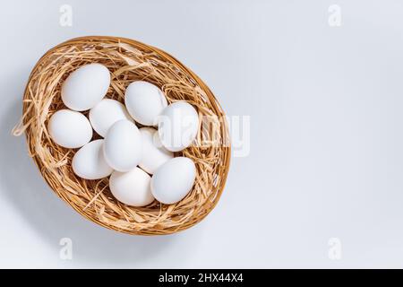White easter eggs in yellow basket with straw on white background. Top view of Happy Easter postcard concept Stock Photo
