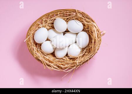 White easter eggs in yellow basket with straw on pink background. Top view of Happy Easter postcard concept Stock Photo