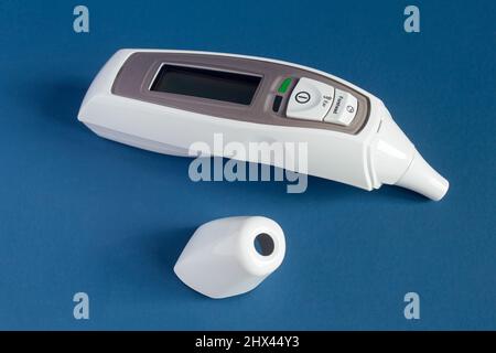 Infrared Forehead and Ear Thermometer with LCD display and fever alarm with the cap removed on a blue-pastel colorful studio background. Healthcare an Stock Photo