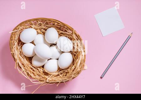 White easter eggs in yellow basket with straw on pink background. Top view of Happy Easter postcard concept Stock Photo