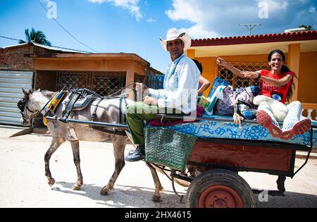 Woman sitting on a horse drawn buggy and a Cuban cowboy ride through the street of Trinidad, Cuba a UNESCO Heritage site. Stock Photo