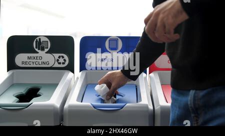 Concept of environment and ecology. Close up of men throwing a pasta box and a receipt into a trash bin used for throwing paper, wrong recycling. Stock Photo
