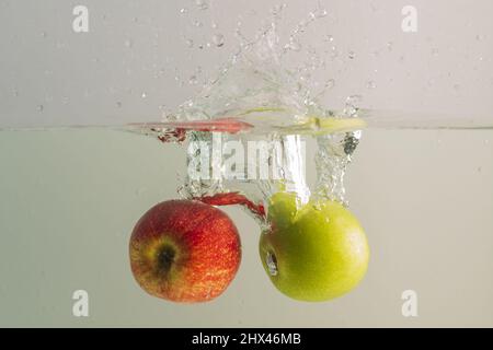 Close up view of falling red and green apples into water. Healthy food concept. Stock Photo