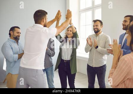 Successful man and woman give each other five when meeting colleagues in bright, spacious office. Stock Photo