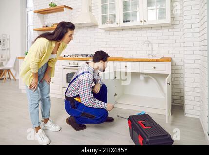 Plumber fixing the problem of a clogged sink pipe in the kitchen of a young woman's house Stock Photo